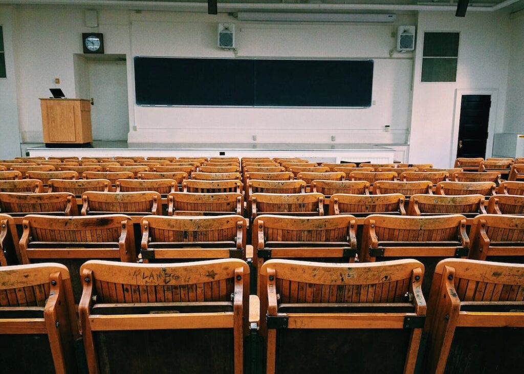 Lo sguardo sull'aula deserta, con file ordinate di sedie rivolte verso lo schermo, racconta più di quanto sembri. È un'istantanea dell'effetto diretto che la progettazione degli spazi ha sui comportamenti. Il rigore e la monotonia di queste aule suggeriscono come progettare uno spazio sia, in realtà, progettare un comportamento, un modello che gli studenti imparano e portano con sé nella vita adulta e lavorativa.