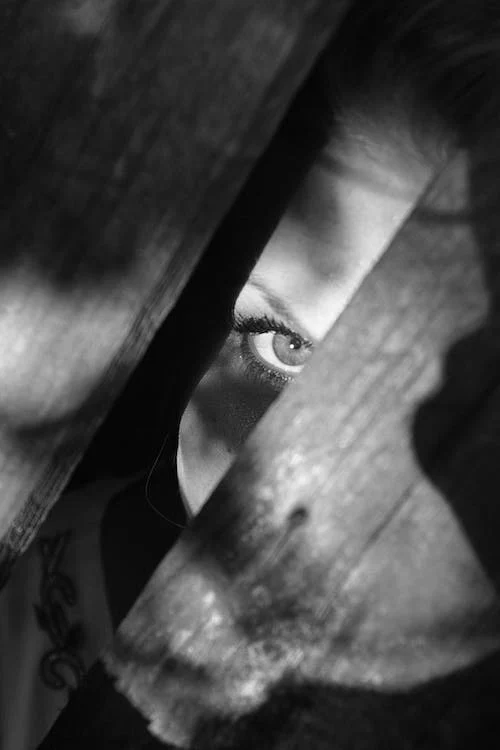 Lo sguardo di questa ragazza attraverso una fessura ricorda qualcuno nascosto dietro le ante di uno spazio buio in un nascondiglio segreto